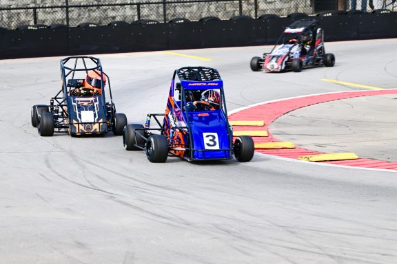 Three small racing karts compete on a curved track, with colorful designs and dynamic motion.